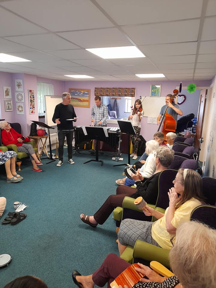 Sinfonia Viva musicians visiting 1 Oak Chilton Daycentre. A Busy room full of daycentre members and musicians playing music and having fun